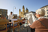 Eine Frau liest Zeitung auf der Terrasse des Café Tambosi, Blick auf Theatinerkirche, Odeonsplatz, München, Bayern, Deutschland