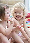 Two three year old girls sitting on the floor, in only pants, laughing
