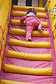 The back of a 3 year old girl climbing up huge inflatable pink steps