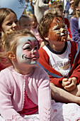 groupp of children sitting on the floor, some with their faces painted