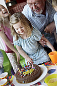 Little girl s third birthday party, looking at her cake with her grandad.