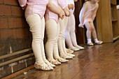 The feet and legs of a group of 3 year old girls in ballet class, dressed in pink leotards and tights, standing in a line