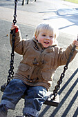 2 year old boy ,on a swing in the park smiling off camera