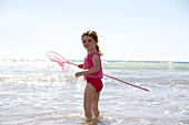 4 year old girl standing in the sea with a fishing net