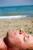 Profile of a 45 year old mans face close up as he sleeps on a beach and sea line behind him