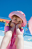 5 year old girl, sitting smiling into camera, wearing a swimsuit and sunhat, at the swimming baths