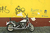 Puerto Rico, San Juan. Motorcycle parked on brick street, colorful wall with graffiti