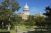 Texas, Austin. Goddess of Liberty hold star atop dome of state capitol building, green space around building, trees, street lamps along sidewalk
