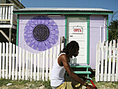 BELIZE Caye Caulker Open sign on white door, small purple building for spa, white picket fence, man bicycle past