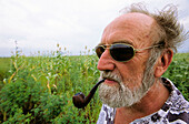 Old man with beard and pipe standing in corn field. India.