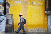 Picture from a man walking in front a painted wall. Antigua Guatemala. Sacatepéquez Region. Guatemala
