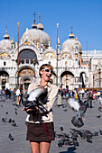 Young woman feeding doves on St. Markus Square, Venice, Veneto, Italy