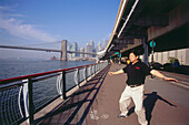 Mann macht Tai-Chi am East River mit Blick auf Brooklyn Bridge, New York, USA, Amerika