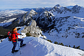 young woman ascending summit ridge of Sebenspitze, lake Forggensee, Schlicke and Gehrenspitze in background, Tannheim range, Allgaeu range, Allgaeu, Tyrol, Austria