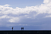 Human figures walking on Victoria breakwater sea wall. Victoria, BC, Canada