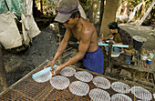 Man rolling out rice paper to dry as woman makes it. Don Teav, Battambang province. Cambodia.