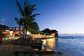 Tourists at promenade next to Pisces Restaurant at night, St. Lawrence Gap, Barbados, Caribbean