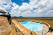 Guests looking over swimming pool to savannah, Voi Safari Lodge, Tsavo East National Park, Coast, Kenya