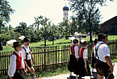 Persons wearing Bavarian costume carrying musical instruments passing, Muensing, Bavaria, Germany