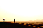 Paar betrachtet Sonnenuntergang in der Wüste, Dubai, Vereinigte Arabische Emirate, VAE