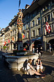 Two young women siting in front of a fountain, Schuetzenbrunnen, Marktgasse, Old City of Berne, Berne, Switzerland