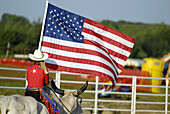 Female cowgirl rides a brama bull carrying flag in the ceremony preceding a rodeo