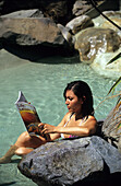 Junge Frau liest Zeitschrift in den heissen Quellen von Hanmer Springs, Südinsel, Neuseeland