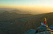 Woman sitting on the edge of a rock watching the sunset, Sayh plateau, Mountain landscape, Hajjar mountains, Kashab, Khasab, Musandam, Oman