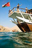 Woman jumping from a boat into the sea, Boat with tourists, Dhow, Haijar Mountains, Musandam, Oman