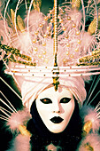 One person in an oriental themed white mask with elaborate feathers at yearly carnival in Venice, Italy