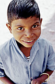 Young Indian boy with a big smile and wet hair wearing a blue shirt looking up.