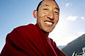 Portrait of one Tibetan Buddhist monk smiling with blue sky as background at low angle. Tibet, China, Asia.