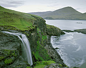 Waterfalls, mountain, green grass, sky. Faroe island. Denmark.