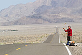 A man juggling while hitch hiking in the desert road near Lone Pine, California. USA