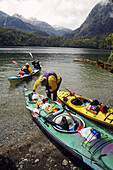 Sea kayakers coming ashore at a wilderness beach in remote Doubtful Sound, Fiordland National Park, New Zealand.