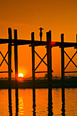 Silhouettes of people walking across the iconic U-Bein bridge over the Taungthaman Lake at sunset, Amarapura, Myanmar. The U-Bein Bridge at 1.2 km. (3/4 of a mile) is the longest teak bridge in the world.