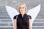 Mid adult woman wearing angel wings in front of a staircase