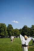 Angel, young woman with wings watching men play football in the park, Munich, Bavaria, Germany