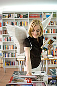 Angel, young woman with wings looking at books in a book shop, Munich, Bavaria, Germany
