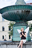 Angel, young woman with wings sitting next to a fountain, University, Munich, Bavaria, Germany