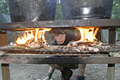 A boy scout checks on the fires he built for heating dish water during summer camp in Missouri. USA.