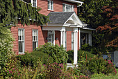 New England cottage surrounded by bushes, flowers and autumn fall trees