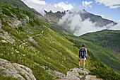 Female hiker pausing on rock outcrop to take in view of the Garden Wall as seen from the Highline Trail in Glacier National Park, Montana, USA