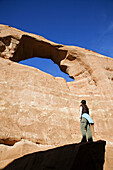 Female hiker viewing Skyline Arch from a large boulder below, Arches National Park, Utah, USA.