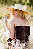 Young blonde woman with apple sitting in green grass