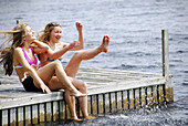 sisters 13 and 18 kicking up water while sitting on dock at lake
