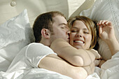 Young couple in bed cuddling and playing together