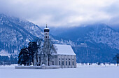 Europe, Germany, Bavaria, Schwangau near Füssen, St. Coloman pilgrimage church surrounded by trees and Neuschwanstein Castle in the mountains