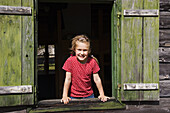 Girl looking out of a window of a wooden hut, Austria