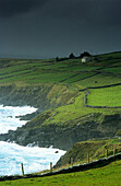 Küstenlandschaft und Häuser unter dunklen Wolken auf der Halbinsel Dingle, County Kerry, Irland, Europa